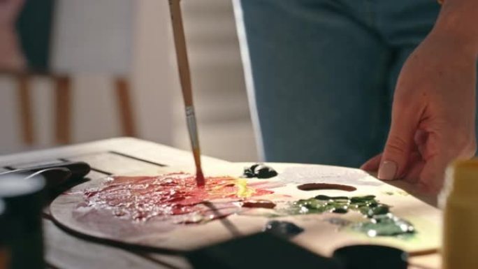 画家手持刷子并在木制调色板上混合油漆的特写镜头。创意艺术家玩弄色彩组合，创造新的色调和纹理，尝试不同