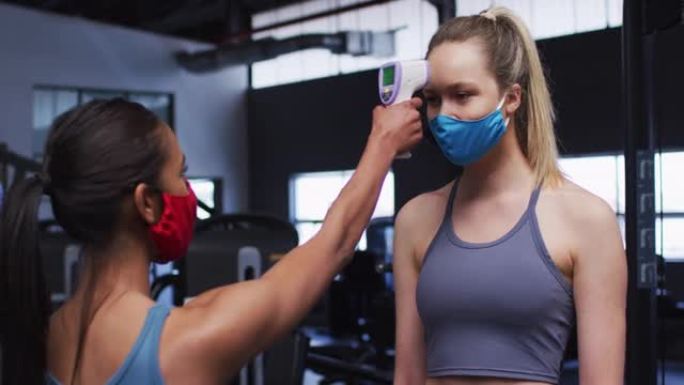 戴口罩的健康白人妇女在健身房测量健康白人妇女的温度