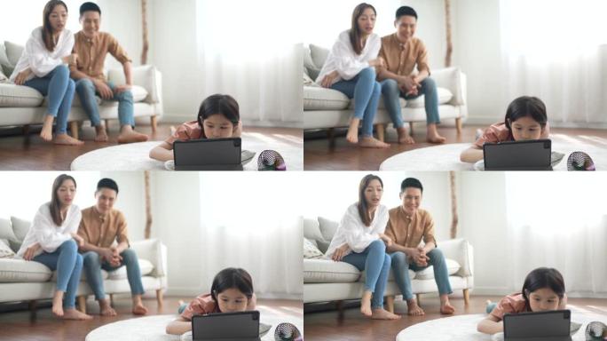 小女孩在家放松时在数字平板电脑上画画，两个父母坐在沙发上