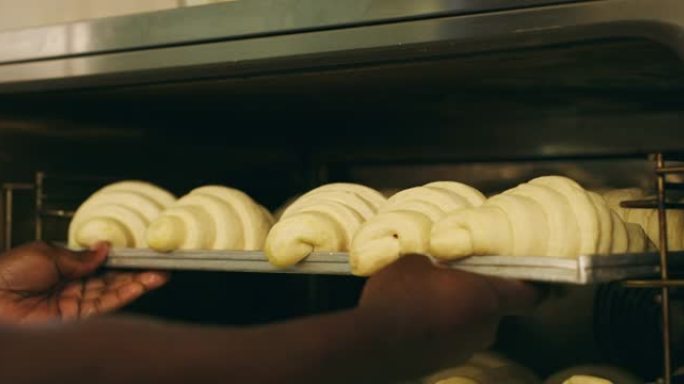 4k视频片段，一个无法识别的人将一盘羊角面包放在面包店的烤箱中