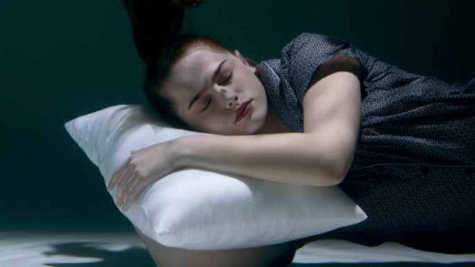 睡着了，穿着睡衣的年轻美女沉入水中，头在白色枕头上做梦慢动作。