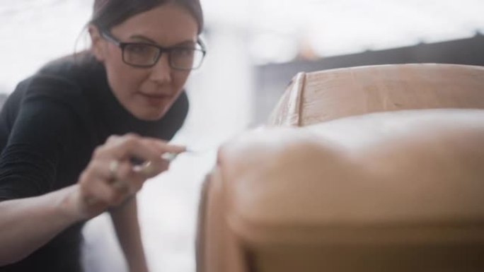 汽车设计师的特写肖像雕刻了现代可持续电动汽车的3D粘土模型。年轻女性使用刮铲仔细修剪原型概念Eco车