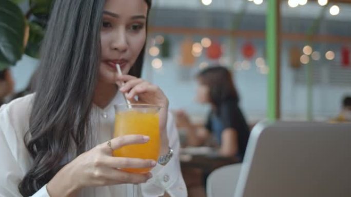 女商人在餐厅使用笔记本电脑并喝橙汁