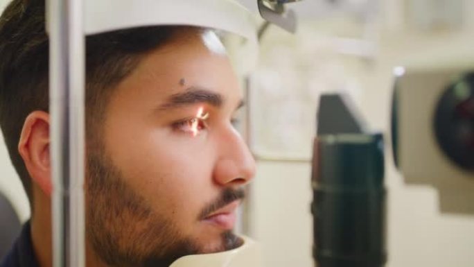 在配镜师咨询期间测试男性患者的眼睛和瞳孔反射的裂隙灯机器的特写镜头。验光师一名男子的头像，用led灯