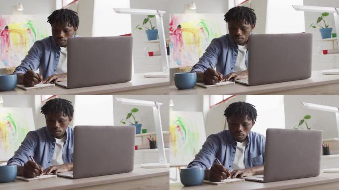 坐在艺术工作室的桌子上的笔记本电脑做笔记的非裔美国男性艺术家