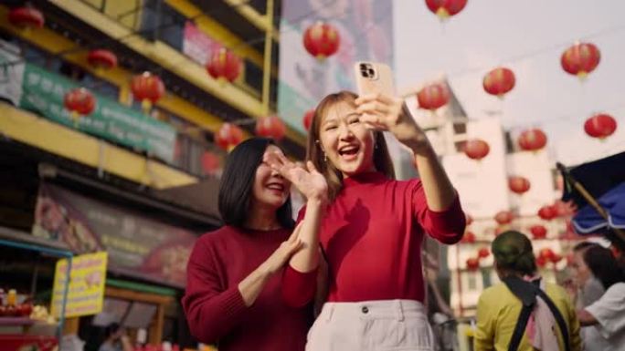 在中国城镇地区的农历新年灯笼上使用电话的亚洲妇女