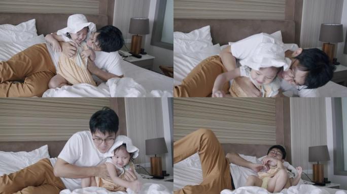 亚洲女儿蹒跚学步的孩子和父亲在床上玩耍。父亲在家里拥抱或拥抱他可爱的女婴。