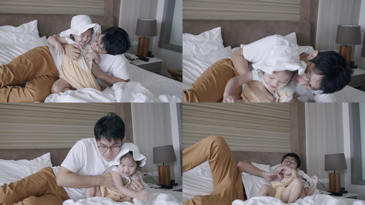 亚洲女儿蹒跚学步的孩子和父亲在床上玩耍。父亲在家里拥抱或拥抱他可爱的女婴。
