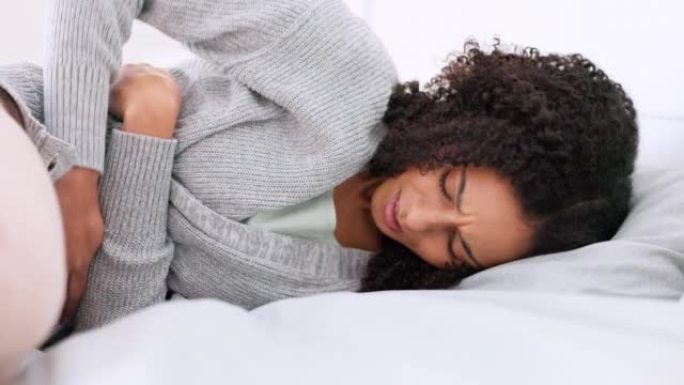 床，胃痛和年轻的女人在肚子上做按摩以缓解月经疼痛的问题。悲伤，生病和沮丧的女孩躺在卧室里时感到腹部痉