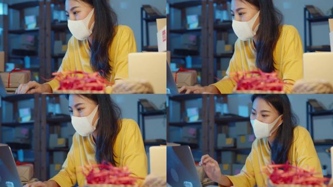 年轻的亚洲女商人戴着口罩检查购买订单，晚上在家庭办公室的笔记本电脑上回复客户收件箱聊天。