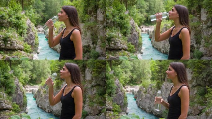 女人在山河休息，用可重复使用的水瓶补水