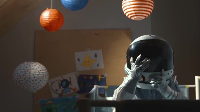 梦见太空旅行。小宇航员孩子坐在床上，穿着太空服和头盔在他的房间里睡觉
