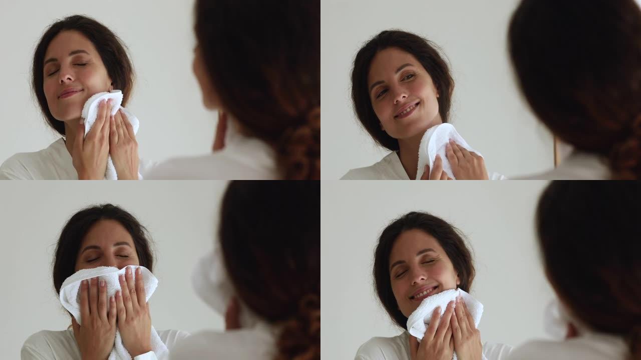 女人在用柔软的毛巾擦脸时照镜子