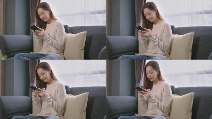 美丽的亚洲年轻女子年龄36岁，早上在家坐在沙发上放松，通过手机工作和网上购物。成人在线学习概念。与A