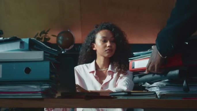 年轻忙碌的混血女财务经理在办公室桌子上工作，老板带来了一堆令人震惊的文件。