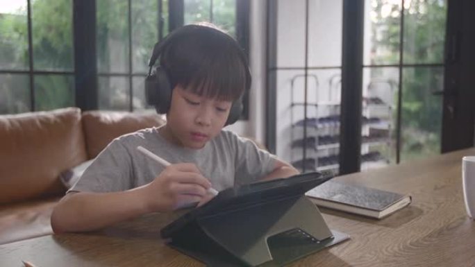 亚洲男孩正坐在家里专心在线学习，他记下了自己所学到的知识。通过笔记本电脑，人们因为covid 19而