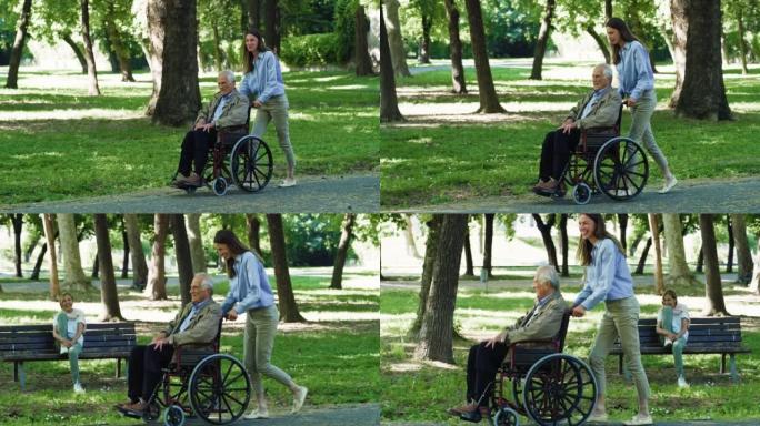 无忧无虑的快乐孙女和坐在轮椅上的祖父在绿色公园一起散步的电影镜头。幸福，自由，生活，祖父母，世代，爱