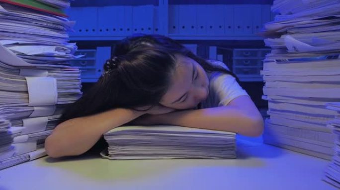 亚洲年轻女性在深夜工作的办公桌上睡觉时过度劳累。新型冠状病毒肺炎在家工作。