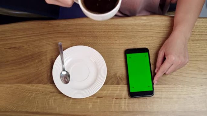 女士无法辨认的女人在家里喝咖啡时使用带有色度键绿屏的智能手机