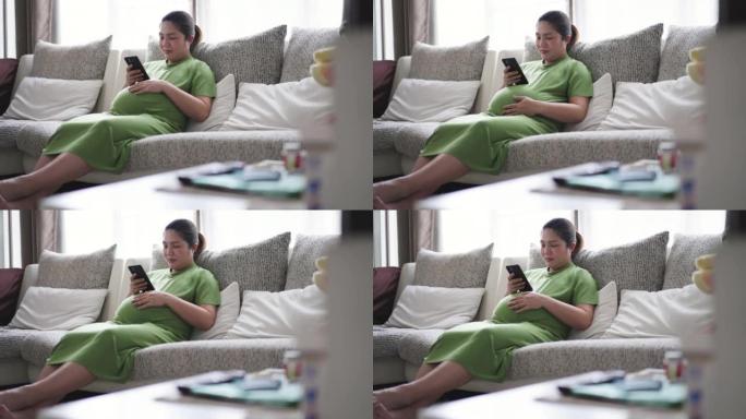 穿着绿色西装的孕妇在家中客厅沙发上使用手机