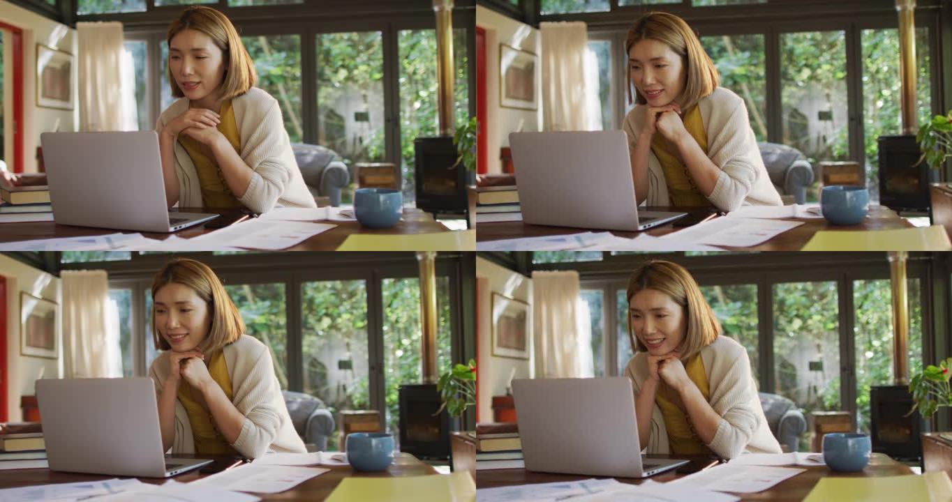 坐在餐桌旁在家工作并使用笔记本电脑的亚洲妇女