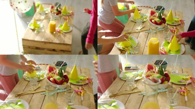 孩子们在餐桌上玩和庆祝生日，吃健康的零食。朋友一边吃水果一边学习试戴可爱的纸帽。兴奋、快乐和顽皮的孩