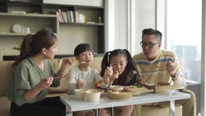 亚洲华人年轻家庭在周末在客厅的电视前享受外卖食物