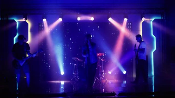 四人摇滚乐队与主唱，吉他手，贝斯手和鼓手在夜总会的音乐会上表演。舞台上明亮多彩的频闪灯前的现场音乐派
