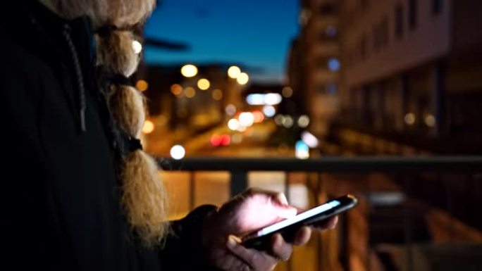 晚上在城市里散步时，无法辨认的留着长胡须的男子使用智能手机