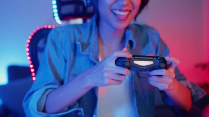 快乐的亚洲女孩游戏玩家戴着耳机和操纵杆控制器与朋友交谈，晚上在霓虹灯客厅家庭工作室的在线游戏中感到有