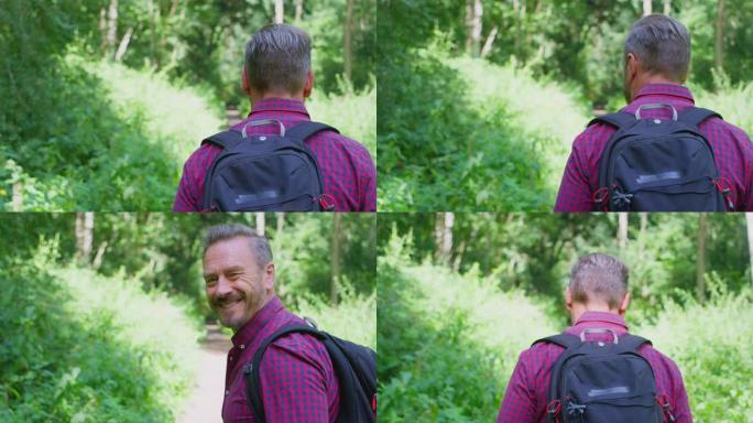 乡下穿着背包的成熟男人沿着森林徒步旅行的后视图