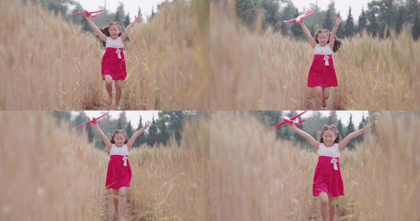 快乐的亚洲小女孩拿着玩具飞机在大麦田里奔跑
