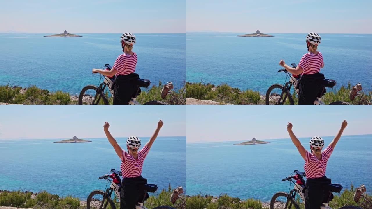 金发碧眼的女人在骑自行车旅行中休息一下，站在赫瓦尔岛的海岸，看着一个小岛，上面有一所房子，将双臂伸向