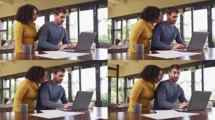 多样化的夫妇在客厅聊天，使用笔记本电脑，看文书工作和支付账单