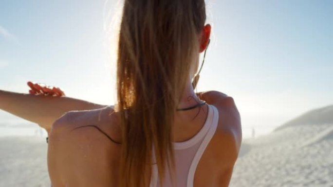 健康活跃的女跑步者通过伸展和听音乐为锻炼训练做好准备。运动员通过在沙滩上运动，同时通过耳机流动，享受