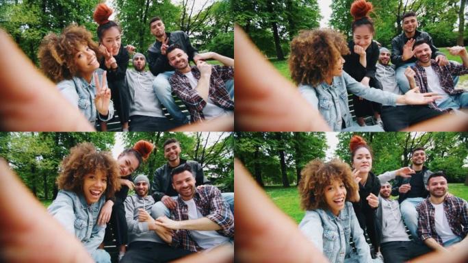在阳光明媚的日子里，一群不同种族的年轻朋友的慢动作在绿色城市公园里玩得很开心，并与手机一起自拍。