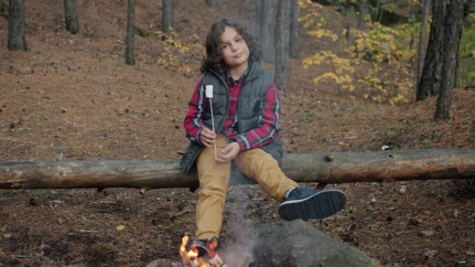 坐在篝火旁拿着烤棉花糖微笑的快乐孩子的慢动作肖像