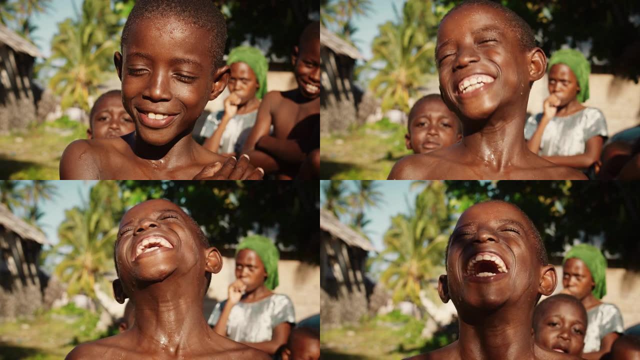 特写一个顽皮的真实的非洲孩子看着相机和其他孩子在背景中笑。快乐活力的黑人男孩与世界分享他美丽的笑容