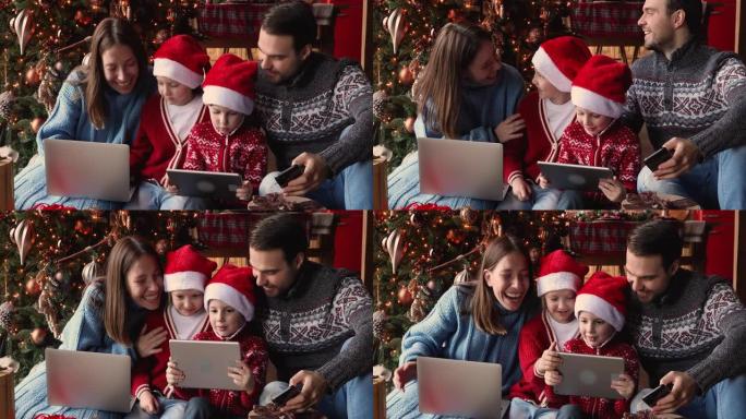 有孩子使用电子设备的家庭坐在圣诞树附近