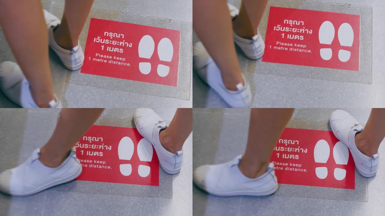 特写亚洲腿站在百货商店地板上的社交距离标志上