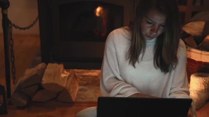 女人在家在壁炉旁使用笔记本电脑时喝杯茶和零食