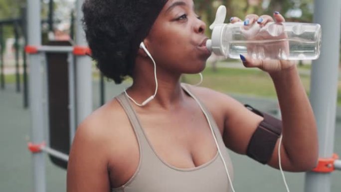 疲惫的黑人女运动员在户外喝水