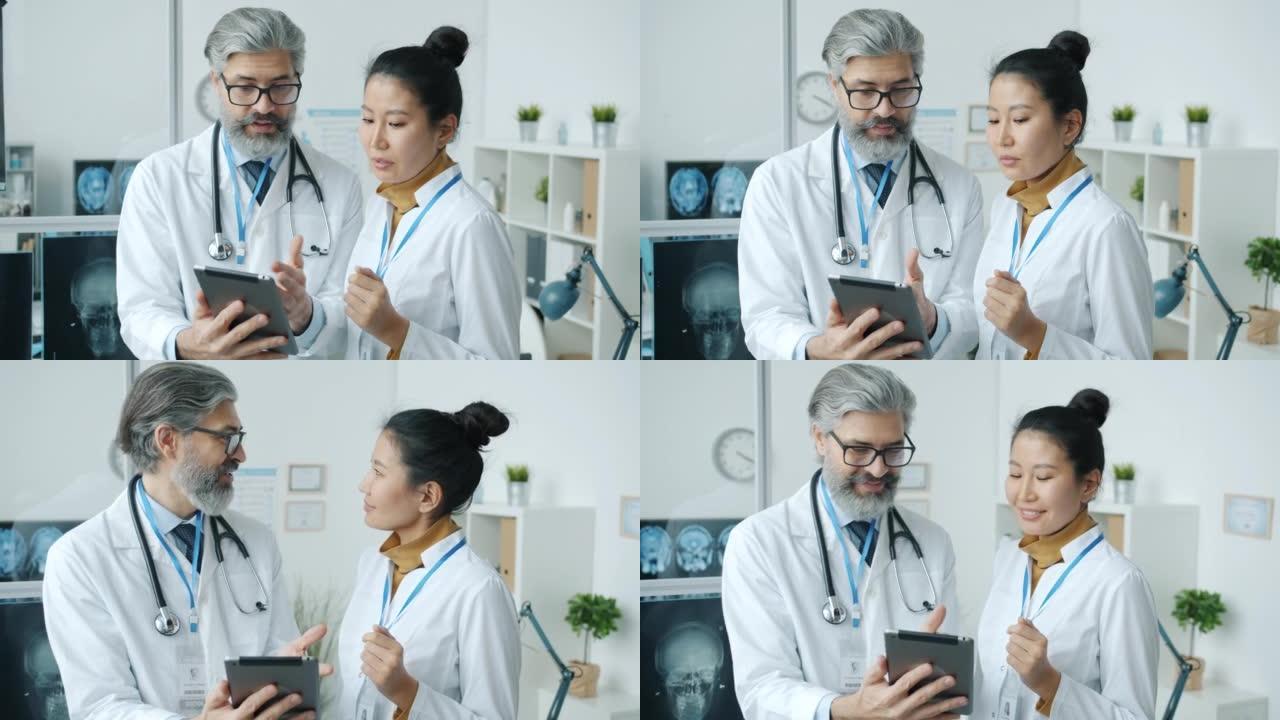 男女医生在现代诊所看着平板电脑屏幕在室内说话和微笑