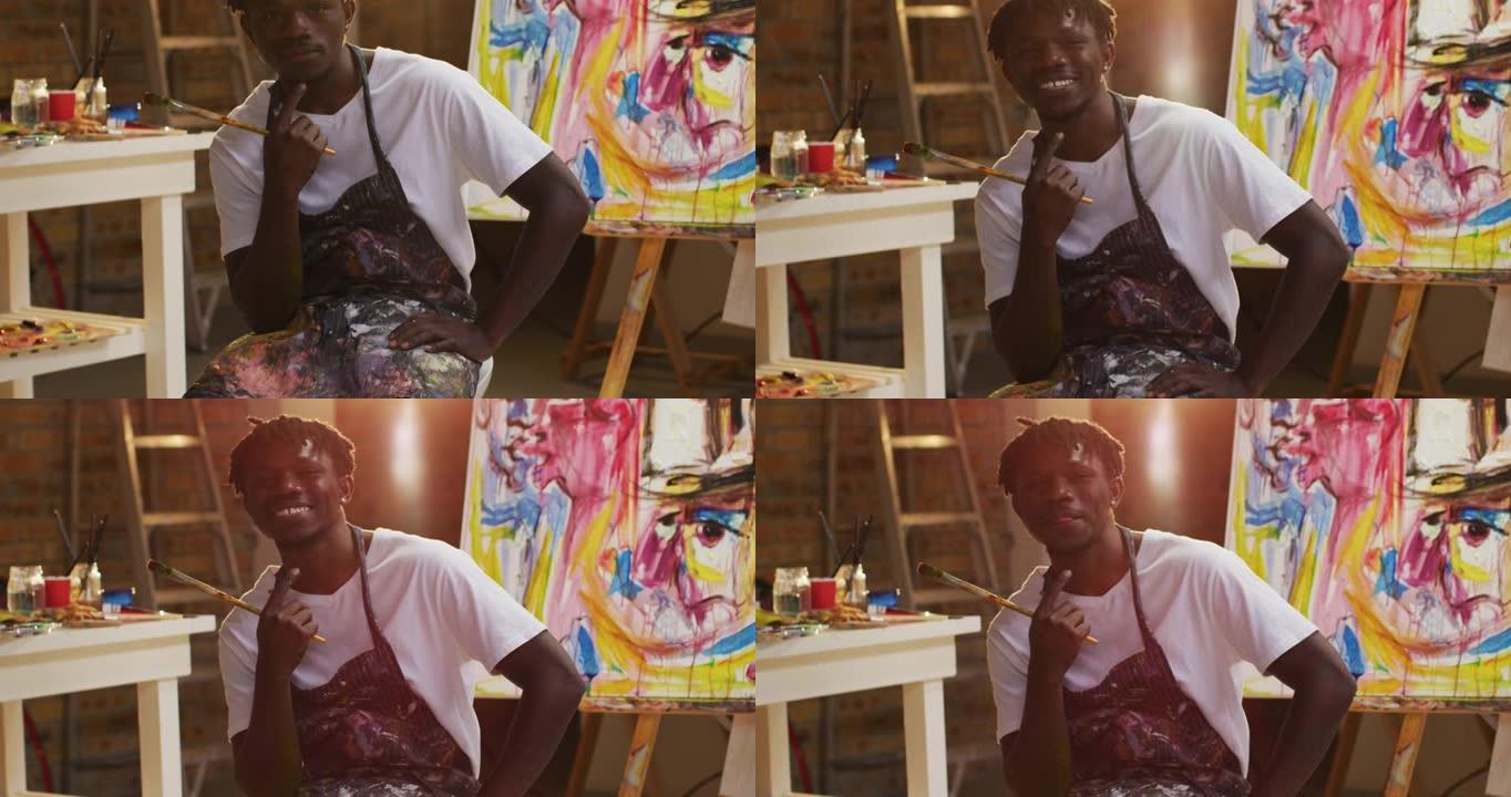 穿着围裙的非裔美国男性艺术家的肖像拿着画笔在艺术工作室微笑