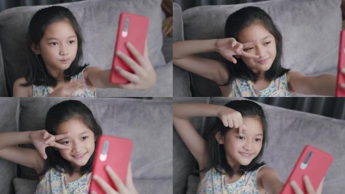 可爱的女孩使用智能手机，在家里自拍时展示心脏手势