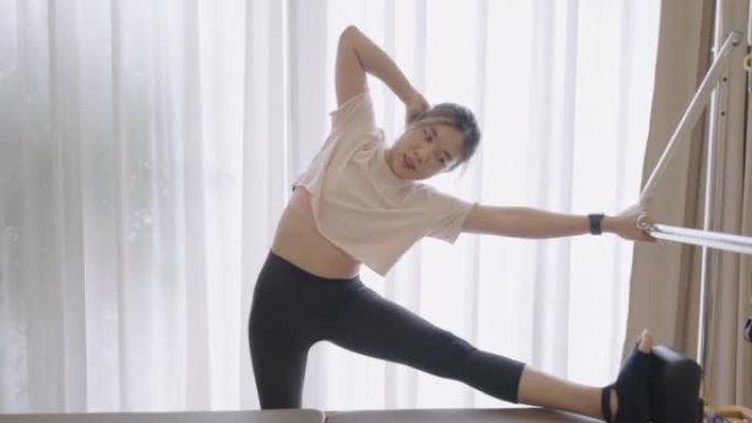 Lean Asian woman on Pilates machine stretching her