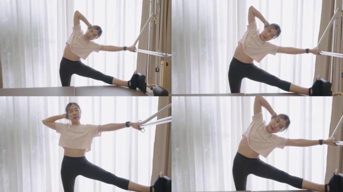 Lean Asian woman on Pilates machine stretching her