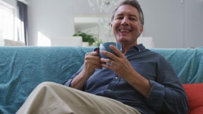 快乐的白人老人坐在客厅喝咖啡和微笑的肖像