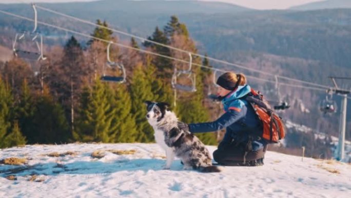 SLO MO年轻女子抱着她的狗在山顶上，可以看到滑雪缆车