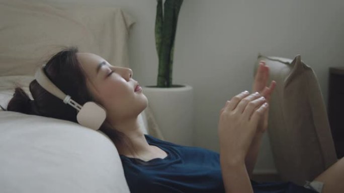 快乐的亚洲女人在卧室里用耳机听音乐。